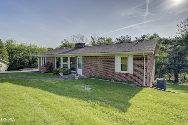 single story home featuring a chimney, cooling unit, a front yard, and brick siding