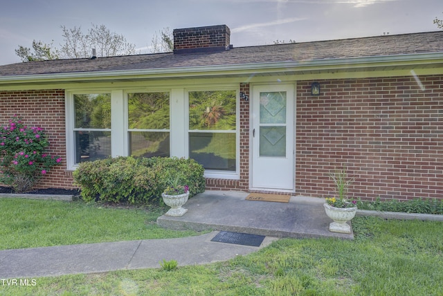 view of exterior entry featuring brick siding, central AC unit, and a lawn
