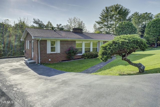 single story home with a chimney, a front yard, and brick siding