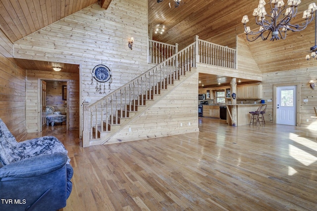 living room featuring wooden walls, high vaulted ceiling, wooden ceiling, wood finished floors, and stairway