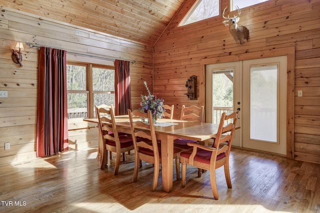 dining room featuring wood walls, wood finished floors, high vaulted ceiling, wooden ceiling, and french doors