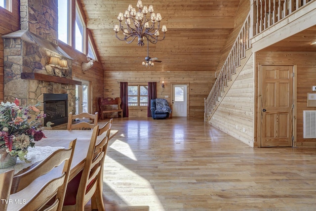 dining room with a fireplace, wood walls, stairway, high vaulted ceiling, and a chandelier