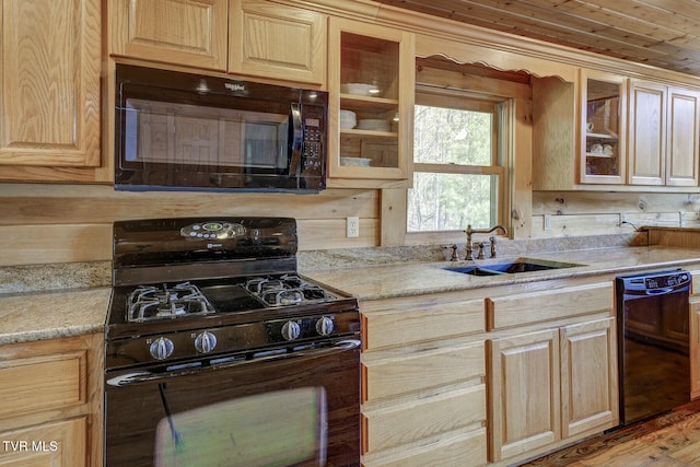 kitchen featuring a sink, light brown cabinets, black appliances, and glass insert cabinets