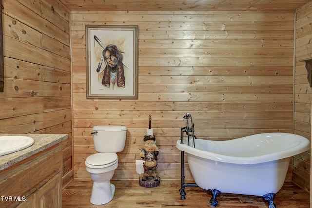 bathroom with wooden walls, toilet, a freestanding bath, and vanity