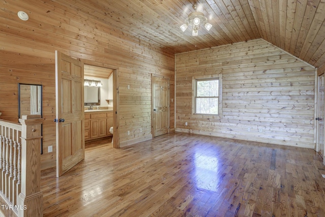 unfurnished bedroom with light wood-style floors, wood ceiling, ensuite bath, and wooden walls