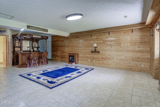 interior space with a textured ceiling, wood walls, bar area, and visible vents