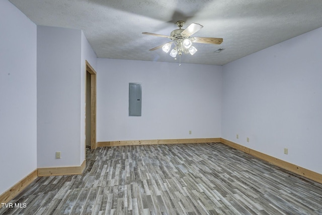 spare room with wood finished floors, baseboards, ceiling fan, a textured ceiling, and electric panel