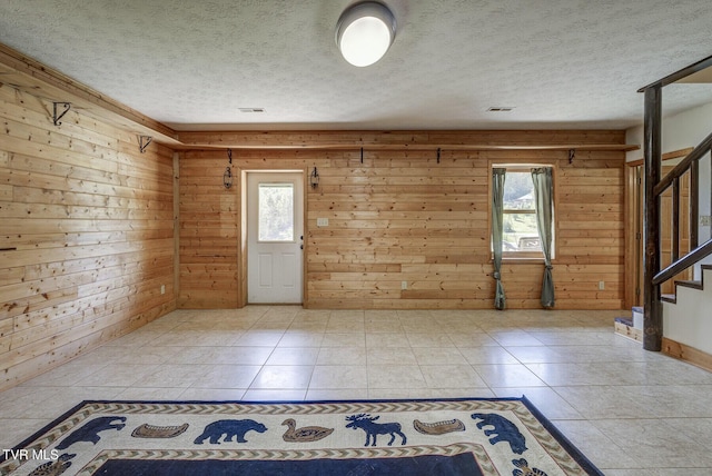 entryway featuring visible vents, light tile patterned flooring, wooden walls, and stairway