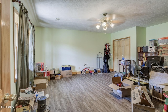 recreation room featuring baseboards, a ceiling fan, a textured ceiling, and wood finished floors