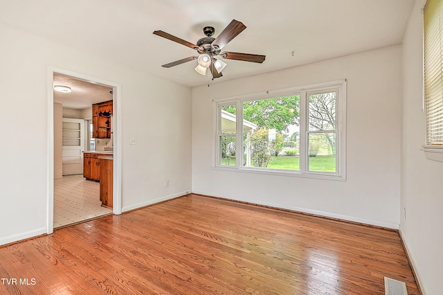 spare room featuring baseboards, ceiling fan, light wood-style flooring, and visible vents