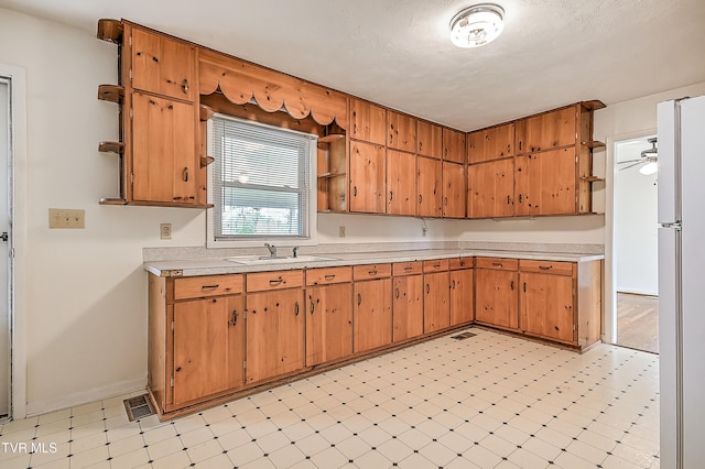 kitchen featuring open shelves, a sink, light countertops, freestanding refrigerator, and light floors