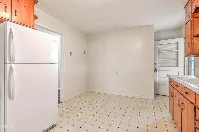 kitchen featuring freestanding refrigerator, baseboards, light floors, light countertops, and brown cabinets