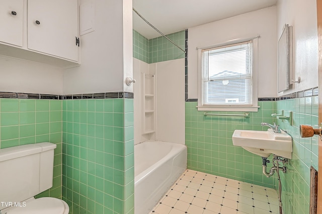 bathroom with shower / bathtub combination, toilet, tile patterned floors, a wainscoted wall, and tile walls