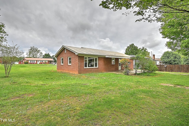 back of house featuring metal roof, a patio area, brick siding, fence, and a yard