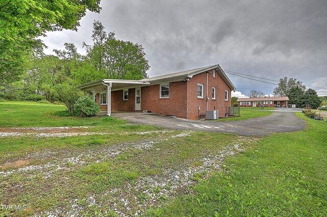 view of home's exterior with central AC, brick siding, a lawn, driveway, and a carport