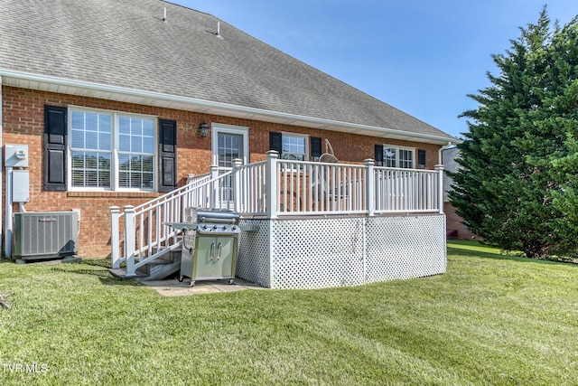 back of house featuring roof with shingles, a lawn, a wooden deck, central air condition unit, and brick siding