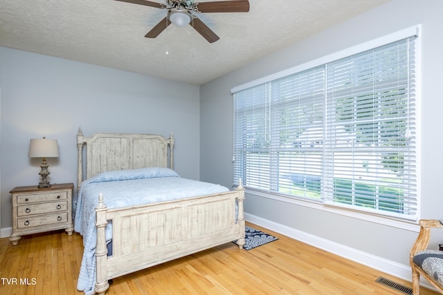 bedroom with ceiling fan, a textured ceiling, baseboards, visible vents, and hardwood / wood-style flooring