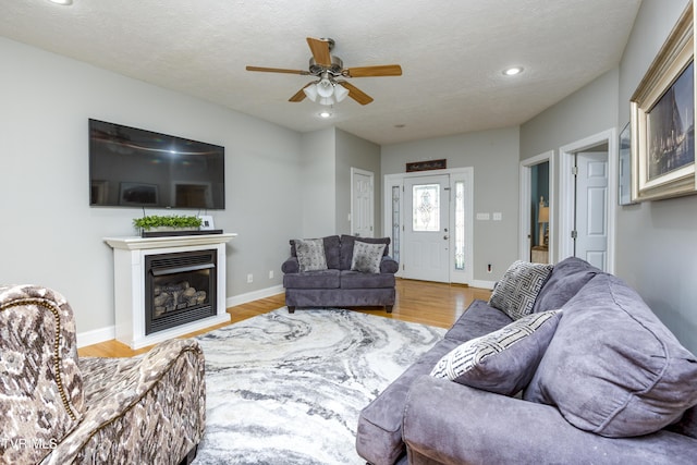 living room featuring recessed lighting, a ceiling fan, a glass covered fireplace, and wood finished floors