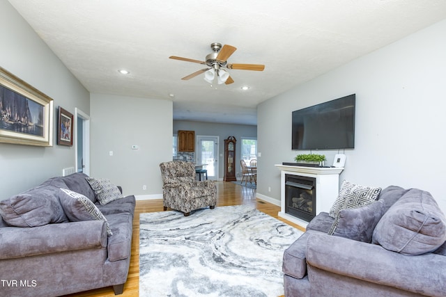 living room featuring ceiling fan, baseboards, light wood finished floors, a glass covered fireplace, and recessed lighting