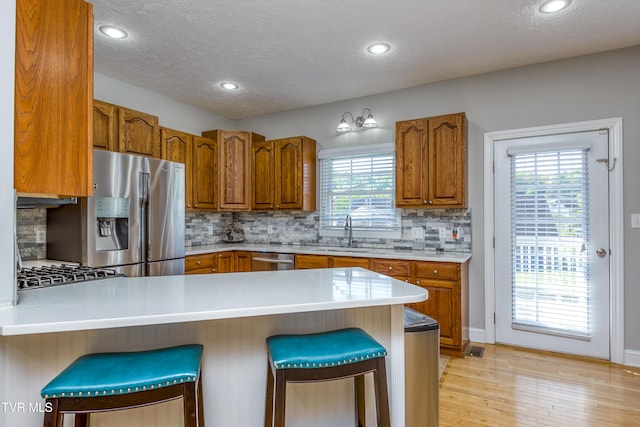 kitchen with brown cabinets, appliances with stainless steel finishes, a sink, a peninsula, and decorative backsplash