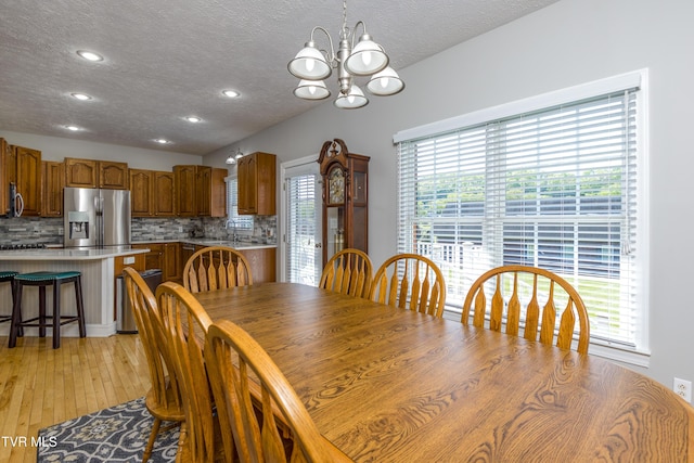 dining room featuring a textured ceiling, a notable chandelier, a wealth of natural light, and light wood-style flooring