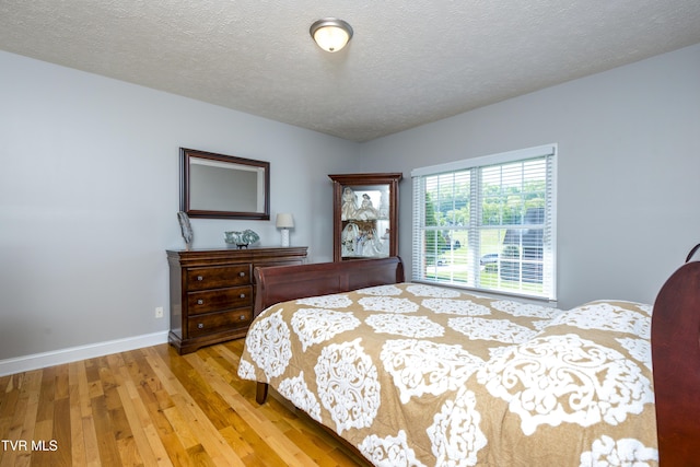 bedroom featuring baseboards, a textured ceiling, and wood finished floors