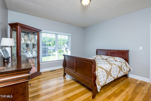 bedroom with a textured ceiling, baseboards, visible vents, and light wood-style flooring