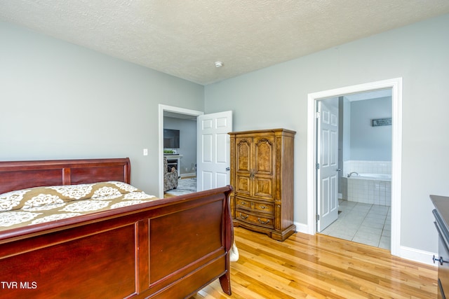 bedroom featuring a textured ceiling, baseboards, ensuite bathroom, and light wood-style floors