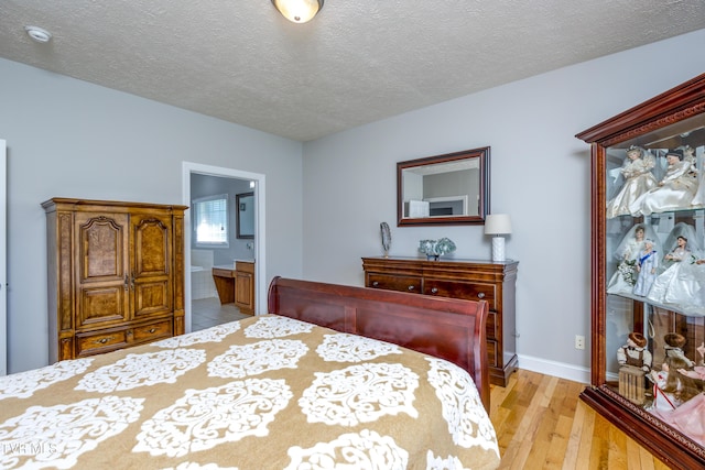 bedroom featuring light wood-style floors, a textured ceiling, ensuite bathroom, and baseboards