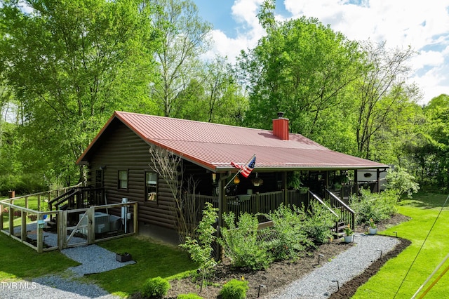 back of house featuring metal roof, a chimney, log siding, a yard, and stairs