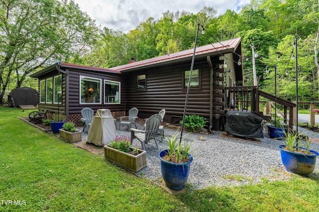rear view of house featuring metal roof, a lawn, log siding, a patio area, and a wooded view