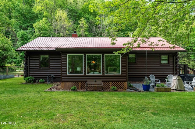 rear view of house with a lawn, a forest view, log exterior, and metal roof