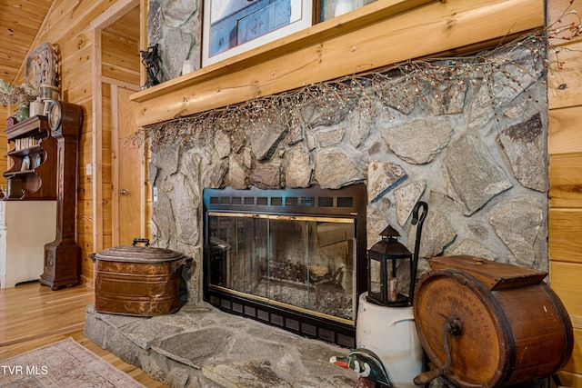interior details featuring a stone fireplace, wood finished floors, and wooden walls