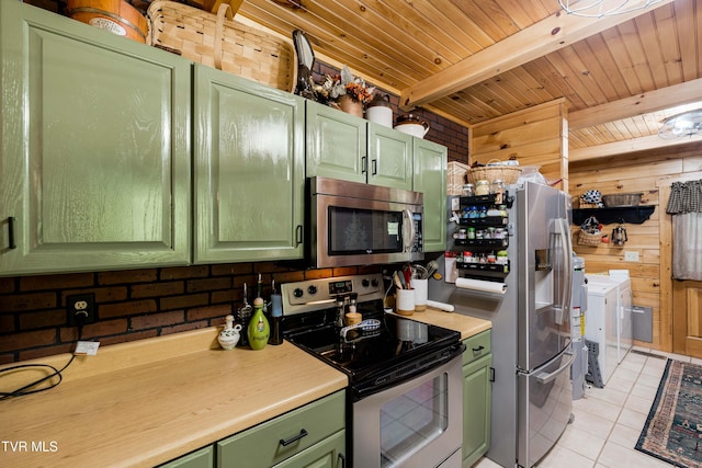 kitchen featuring green cabinetry, appliances with stainless steel finishes, wood walls, light tile patterned floors, and washer and clothes dryer