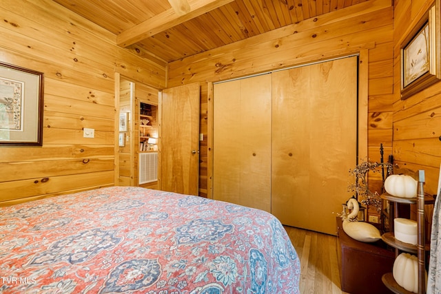 bedroom featuring a closet, wood walls, wood finished floors, beam ceiling, and wood ceiling
