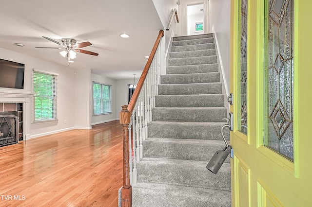 staircase with ceiling fan, a fireplace, wood finished floors, baseboards, and recessed lighting