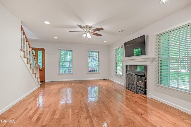 unfurnished living room with ceiling fan, a fireplace, light wood-type flooring, stairway, and baseboards