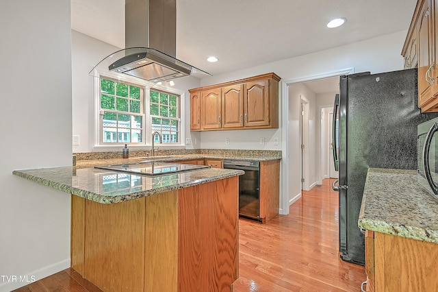 kitchen with a peninsula, island exhaust hood, stone counters, light wood finished floors, and black appliances