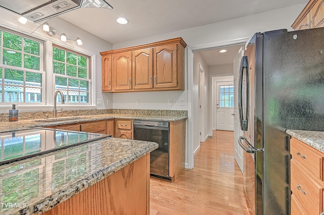 kitchen featuring light stone countertops, a sink, light wood-style floors, freestanding refrigerator, and black dishwasher