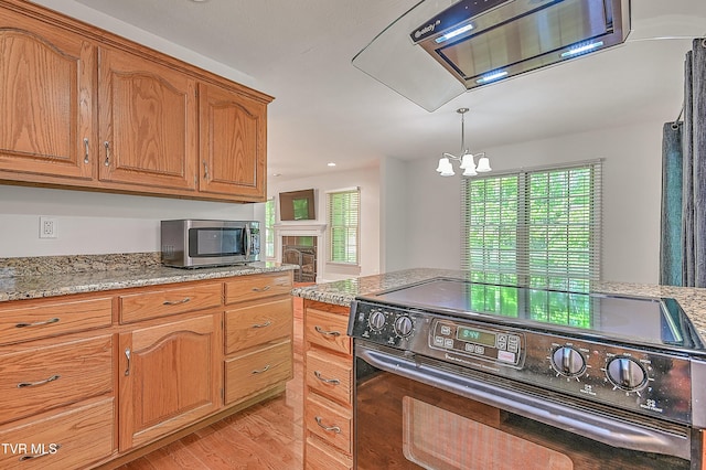 kitchen featuring brown cabinetry, black range with electric cooktop, stainless steel microwave, a chandelier, and light wood finished floors