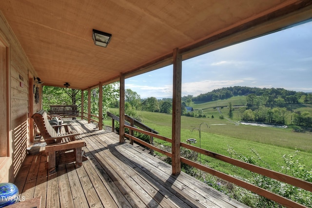wooden terrace with a lawn, covered porch, and a rural view