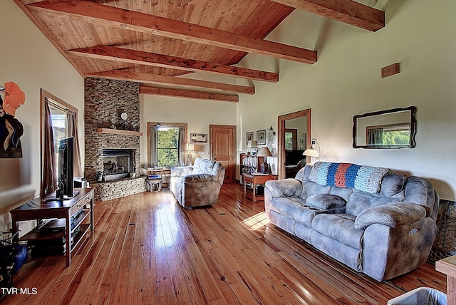 living area featuring wood-type flooring, a towering ceiling, beamed ceiling, a stone fireplace, and wooden ceiling