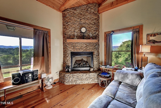 living area with a stone fireplace, wooden ceiling, vaulted ceiling with beams, and hardwood / wood-style flooring
