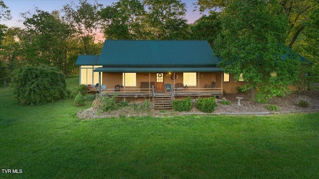 back of house at dusk featuring covered porch, a lawn, and metal roof