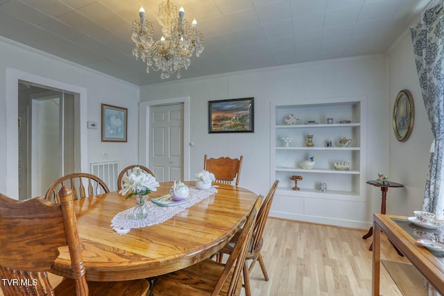 dining space with a chandelier, built in shelves, light wood-style flooring, visible vents, and ornamental molding