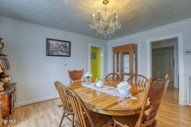 dining space with an inviting chandelier, ornamental molding, and light wood-type flooring