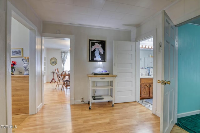 hall featuring crown molding, baseboards, and light wood finished floors