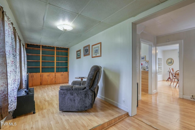 sitting room featuring light wood-style floors, built in features, baseboards, and a paneled ceiling
