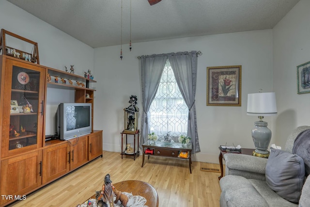living room featuring light wood-style floors, a textured ceiling, baseboards, and visible vents