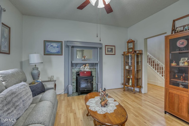 living room featuring light wood-style floors, ceiling fan, stairway, and a wood stove